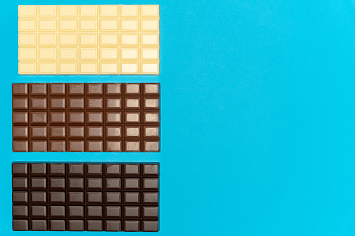 Full bars of dark, milk and white chocolate on a blue background. High quality photo