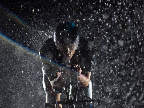 A triathlete braving the rain as he cycles through the night, preparing himself for the upcoming marathon. The blurred raindrops in the foreground and the dark, moody atmosphere in the background add to the sense of determination and grit shown by the athlete un triatleta desafiando la lluvia mientras pedalea durante la noche, preparándose para el próximo maratón. las gotas de lluvia borrosas en primer plano y la atmósfera oscura y cambiante en el fondo se suman a la sensación de determinación y determina