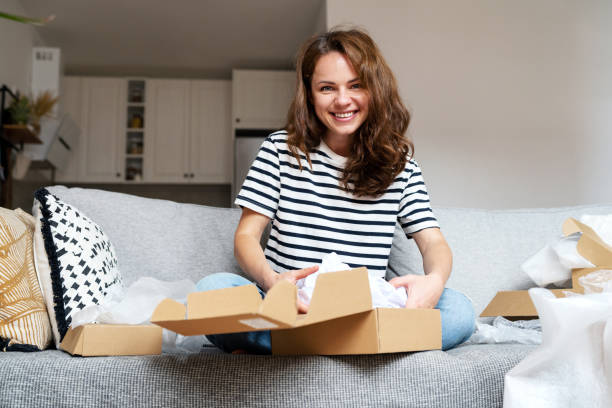 istock Curly woman unpacking a package, opening a cardboard box with online purchases. 1483319328