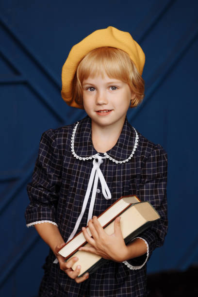 Smiling active excellent student schoolgirl with a book. A child in a school uniform on a blue background.