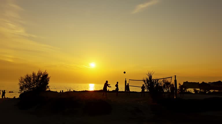 Silhouette friends playing volleyball at beach during sunset