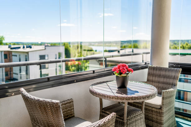 Balcony in summer. Home patio with a view. Condo apartment in city. Scandinavian decor and furniture design. Glass windows, glazing. Flower or plant on table and chairs. stock photo