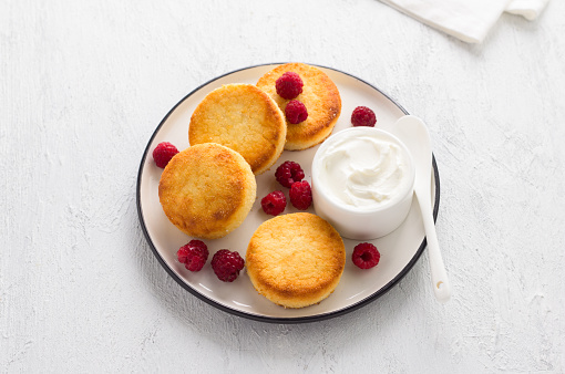 Delicious healthy baked keto syrniki with coconut flour served with sour cream and raspberries on light gray background, top view