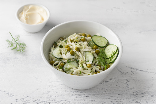 Salad with white cabbage, green peas, cucumber, herbs and mayonnaise sauce on a light blue background. Delicious homemade food