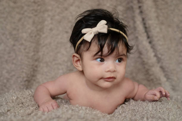 Three month old baby girl wearing only a hairbow during tummy time