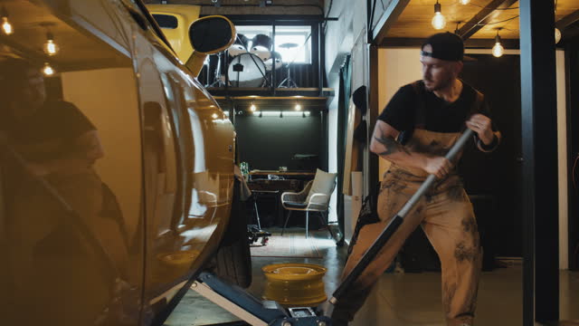 Mechanic Lifting Yellow Car Body With Ram, Standing In Garage, Daytime
