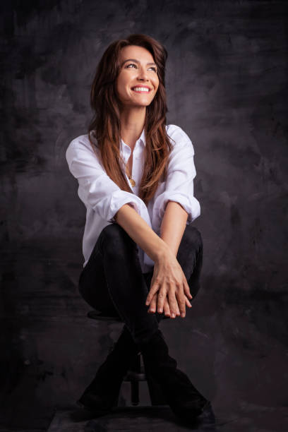 Smiling brunette businesswoman wearing white shirt and laughing against black background stock photo