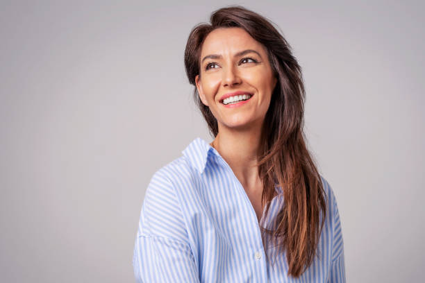 retrato de estudio de una mujer atractiva con camisa y riendo mientras está sentada en un fondo gris aislado. - mirar hacia arriba fotografías e imágenes de stock