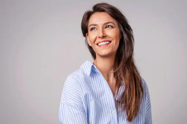 Smiling brunette businesswoman sitting against gray background. Confident female professional is wearing blue shirt. She is having brown hair. Copy space.