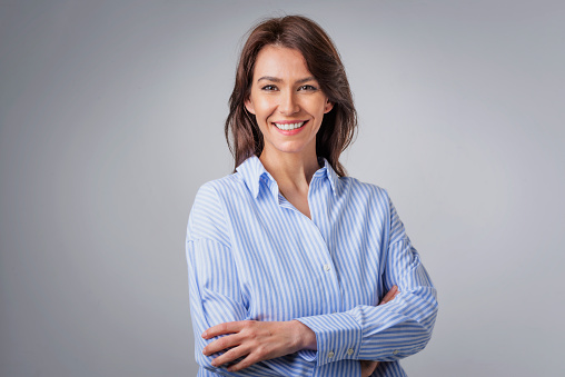 Portrait of cheerful mid adult woman wearing casual smiling at camera. Studio shot, grey background.
