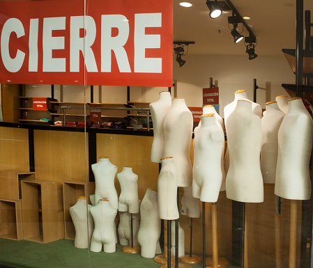 Child and adult group of mannequins in store window with closing sign in spanish language. Galicia, Spain.