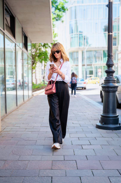 istock Middle aged woman messaging smartphone while walking on street 1483335714