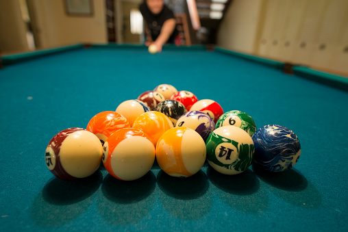 Closeup view of billiard balls lined up for the player at the head of the table to break and start the game. She is waiting to shoot with the pool cue while playing in a basement on vacation.