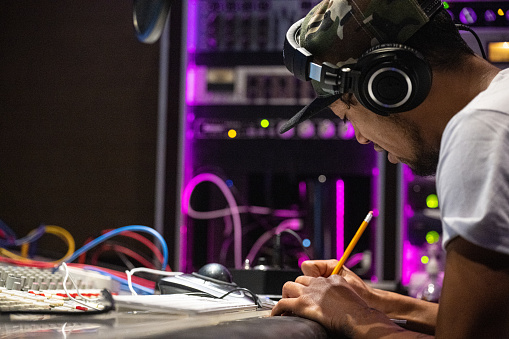 In a modern recording studio, a young New Zealand rapper using a pen and a piece of paper to create his own song. A inspiring and concentrate moment.