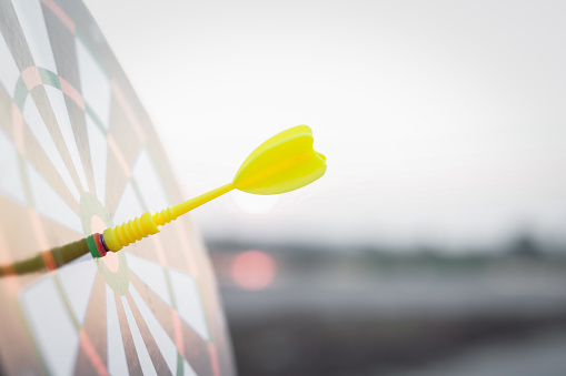 Close up yellow dart arrow hitting target center dartboard on sunset background. Business targeting and focus concept.