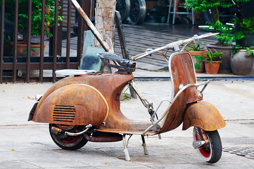 Old rusty Vespa motorcycle parked on sidewalk in front of a shop in street Chokchai 4 in Bangkok Ladprao