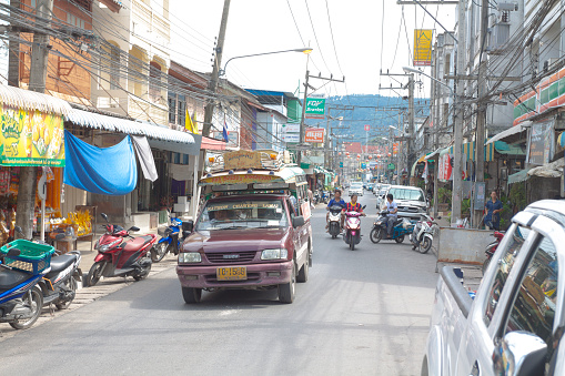 Street with some traffic on Ko Samui in town Nathon at west coast of island. In foreground is a local pick-up taxi, a sangtheaw. In background some people are driving motorcycle.