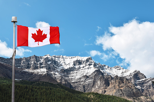 Canadian flag with mountains covered in snow and blue sky in the background