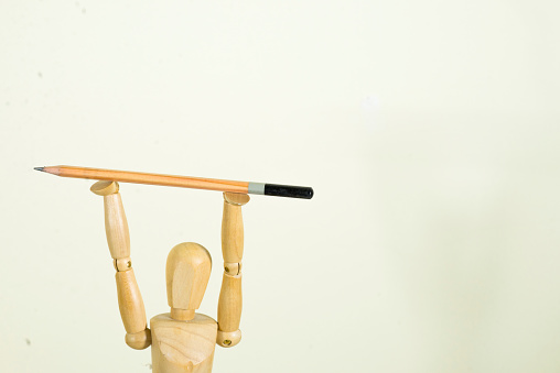 Wooden modelling dummy holding up an artists drawing pencil above its head on a white background.
