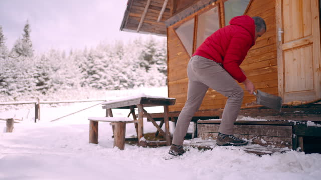 Cabin getaway. Man cleaning snow of log cabin.