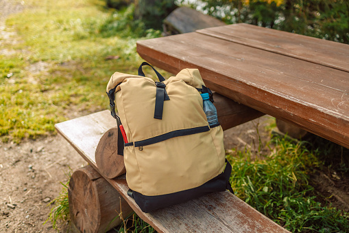 A closeup of a backpack and a water bottle on a bench in the mountain park. High quality photo