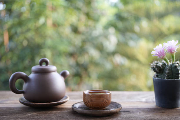 Earthenware teapot and tea cup and pink cactus flower on wooden table