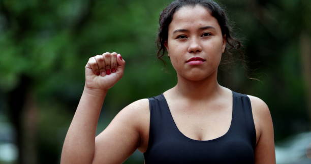 Determine hispanic young woman showing female empowerement signal raising fist stock photo