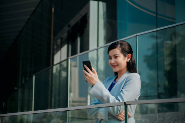 istock Asian Businesswoman sale manager holding and using mobile phone texting message while walking at business district 1483358393