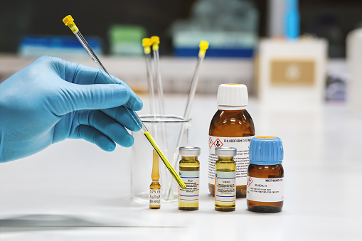 Hand of the scientist shows yellow sample solution was prepared in the NMR glass tubes for analysis by the NMR spectroscopy method. NMR solvent glass bottles, chloroform, pyridine, DMSO, D2O, and methanol.