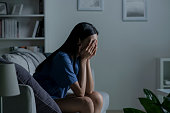 Young Asian woman sitting on sofa at home feeling sad tired and worried suffering depression in mental health.