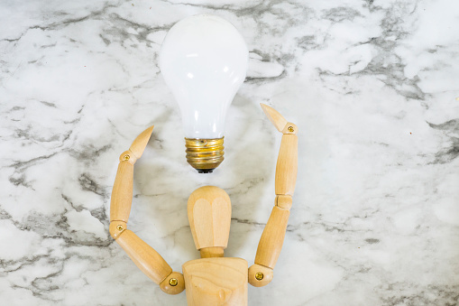 Wooden drawing reference mannequin holding a light bulb above its head to suggest having a creative idea on a plain white background with copy space.
