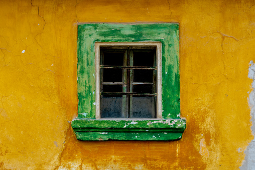Photo of facade of old house with green window and yellow wall.