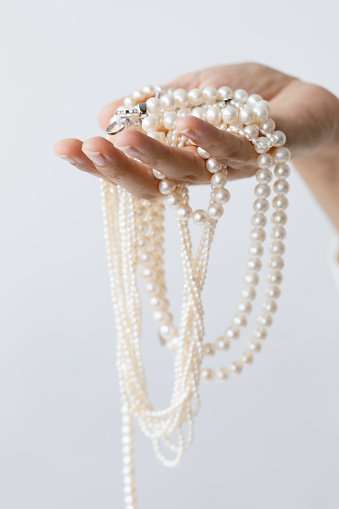 Hand of unrecognizable female is holding white pearl necklaces in front white background.