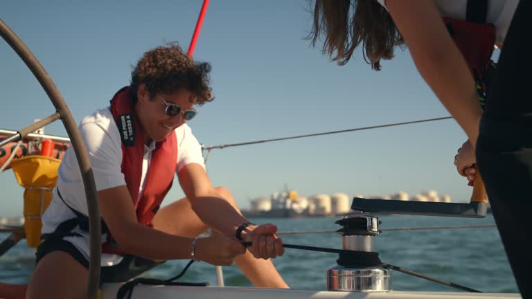 Yacht, sailing and friends hauling winch or rope for travel, adventure or journey on sea or crew. Young people together to work on sailboat or boat rig for transportation, weather or freedom on ocean