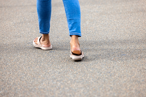 Closeup rear view of young woman legs with flip-flops walking in city, background with copy space, full frame horizontal composition