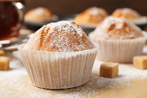 Tasty muffin powdered with sugar on table, closeup