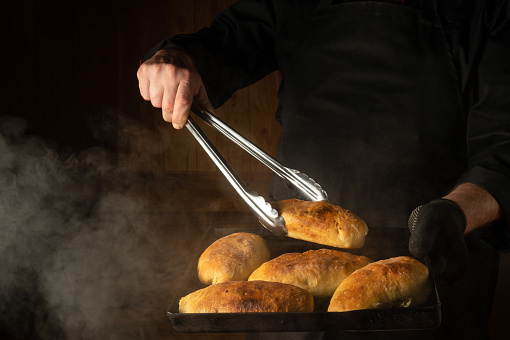 Oven baked buns on a hot baking sheet in the chef hand in glove. The chef takes a hot bun with a culinary tongs.