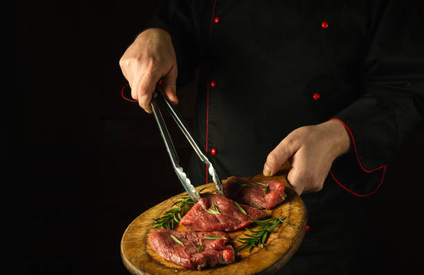 istock The chef holds a cutting board with raw beef steaks before barbecue. Preparation for roasting meat with rosemary and spices. Dark space for restaurant recipe or hotel menu 1483377027