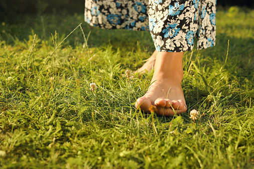 Woman walking barefoot on green grass, closeup. Space for text