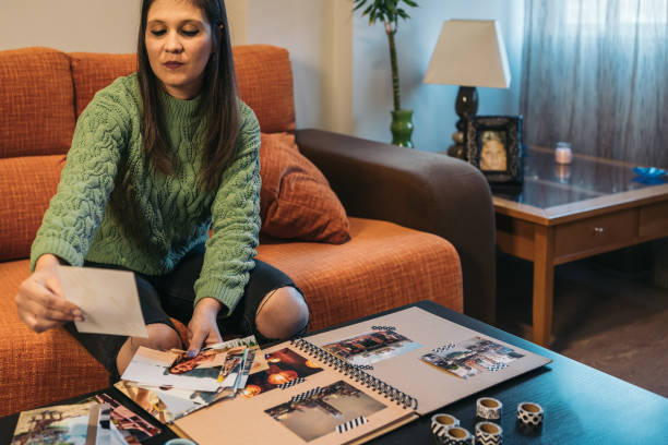 femme brune d’âge moyen regardant sérieusement et avec envie les photos qu’elle utilisera pour faire les pages de son album de voyage kraft fait à la main avec du ruban washi. - longingly photos et images de collection