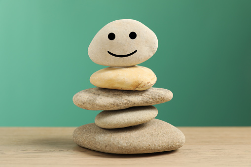 Stack of stones with drawn happy face on table against turquoise background, closeup. Zen concept