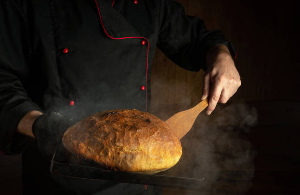 istock The baker bakes bread on a sheet pan in a bakery. Scraper in the chef hand. Place for menu or recipe on dark background. 1483377420