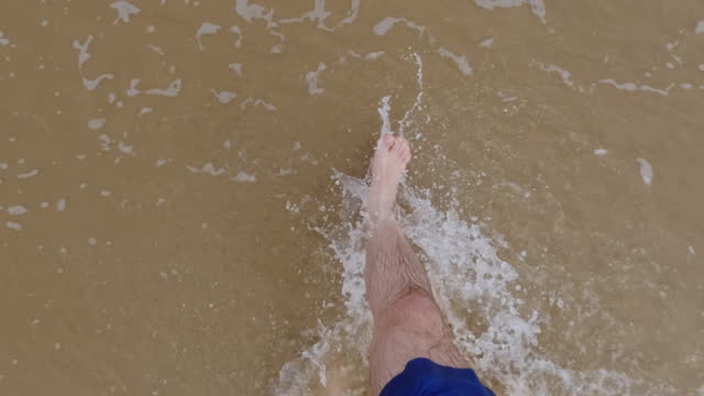 Male legs walking near ocean, stepping at the sand at sea beach. top view