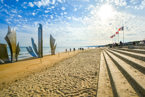 Tourists sit under flags on the steps along sandy Omaha Beach in front of the Les Braves Memorial, site of the World War 2 invasion.