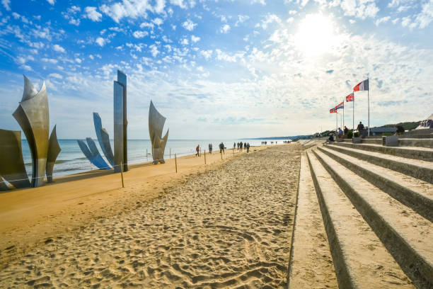 turyści siedzą pod flagami na schodach wzdłuż piaszczystej plaży omaha przed les braves memorial, miejscem inwazji 2 wojny światowej. - omaha beach zdjęcia i obrazy z banku zdjęć