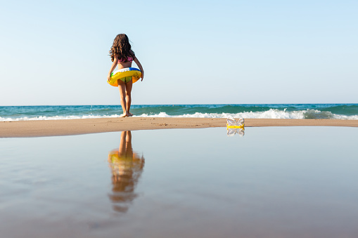 Little girl standing on the beach with inflatable ring and looking at the sea
