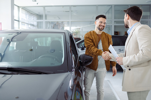 Man buying a new car in car dealership. Handshake and good deal