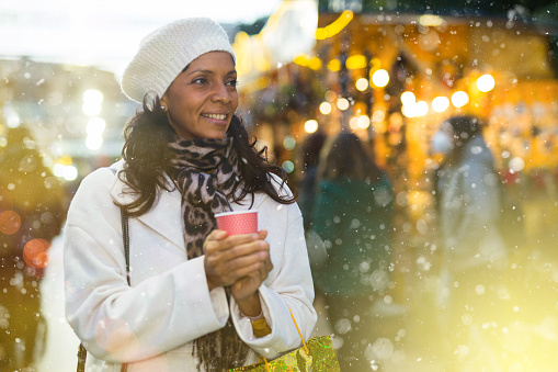 Happy woman holding hot cup of coffee in hands at street christmas fair