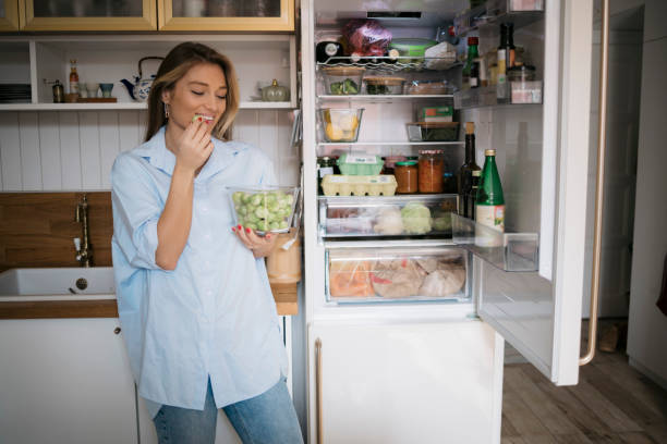 istock Happy young woman eating brussels sprouts standing by open fridge in kitchen 1483385836
