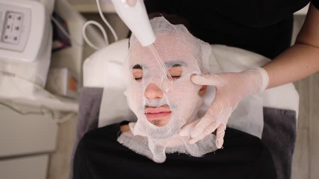 Man receiving facial treatment from an female Caucasian beautician